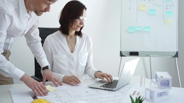 Architects collaborating on building design, reviewing blueprint plans and architectural models, creating detailed floor layout sketches in a professional office environment