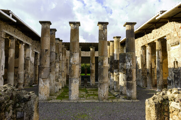Ruins of the Temple of Jupiter in Pompeii, Italy, with ancient columns and stone walls under a cloudy sky. © Nick