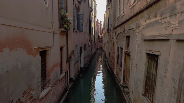 Narrow Venetian canal with calm green water reflections