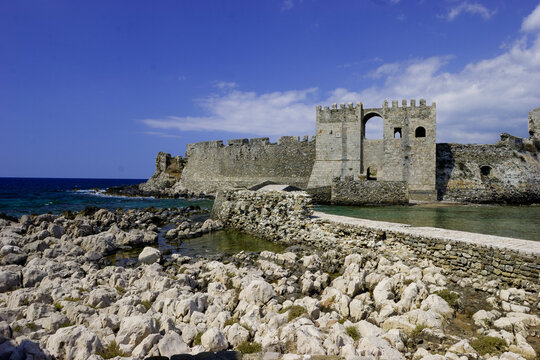 The Methoni Castle, a historic fortress on the coast of Greece, stands under a clear blue sky with scattered clouds.