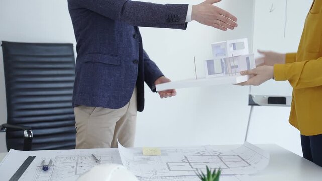 Architect handing over a modern house architectural model to a client, discussing innovative design concepts and construction project blueprints at the office