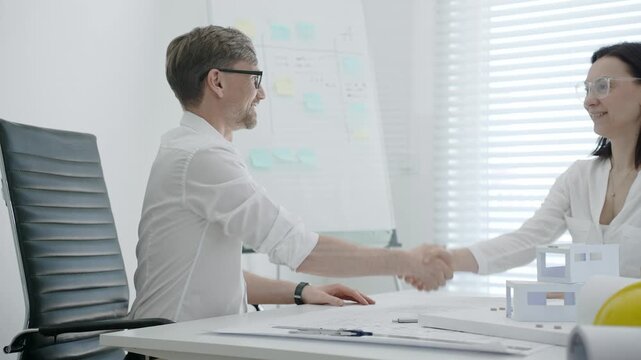 Business partners shaking hands in an architectural office, collaborating on a new construction project, forming a successful agreement and partnership for urban development