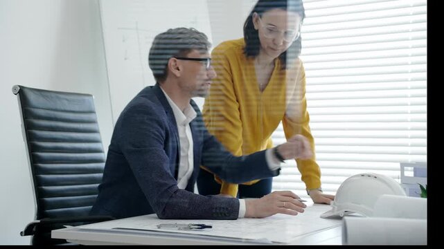 Architects and engineers reviewing blueprints and project plans at a desk, collaborating on design solutions and construction strategy in a modern professional office setting