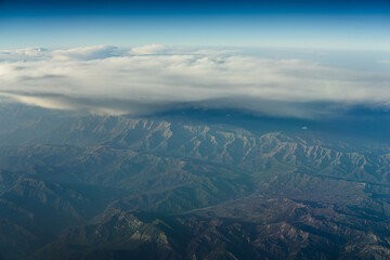 Fototapeta premium Mountains and clouds seen from high altitude during a flight