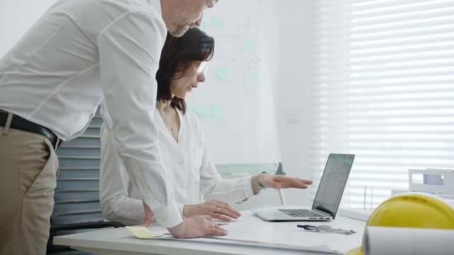 Architects collaborating on building design, reviewing blueprint plans and architectural models, creating detailed floor layout sketches in a professional office environment