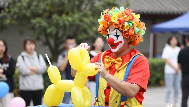 Cheerful clown twists a yellow balloon animal into a dog at an outdoor event