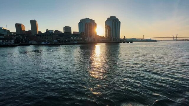 Experience the breathtaking beauty of Halifax Bay at sunset from a ferry, as golden rays reflect on calm waters and cityscape silhouettes dance in the light