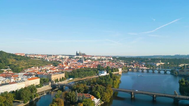 Enjoy a stunning summer morning view of Prague. The city comes alive as sunlight glistens on the Vltava River, showcasing bridges and lush greenery along the embankment.