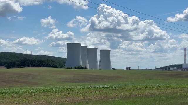 close up view of four massive concrete cooling towers of a nuclear power plant emitting white steam against a blue sky with clouds