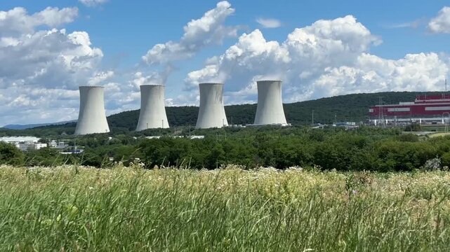 close up view of four massive concrete cooling towers of a nuclear power plant emitting white steam against a blue sky with clouds