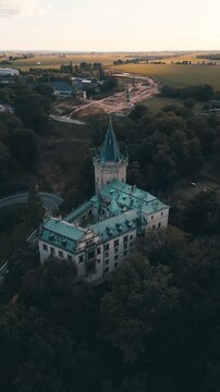Stranov Castle stands amidst green fields and wooded areas. The drone captures its unique architecture and the surroundings in a clear evening light.