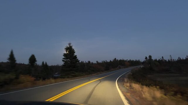 View from car window on winding road at dusk near Peggy's Cove with moon and forest