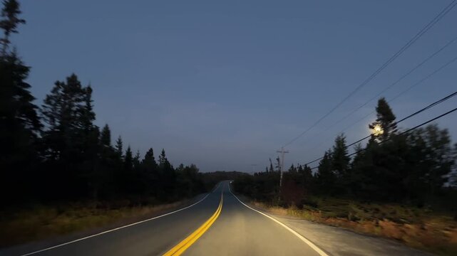 View from car window of winding road at Peggy's Cove with ocean and moon near Halifax at dusk