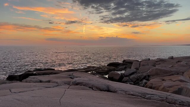 Waves crash on the rocky shore of Peggy's Cove as the sun sets over the Atlantic Ocean. The colors shift in the sky as evening approaches