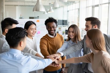 Obraz premium Diverse group of six colleagues forming a cohesive circle, all placing their hands together in the center, symbolizing unity and teamwork.