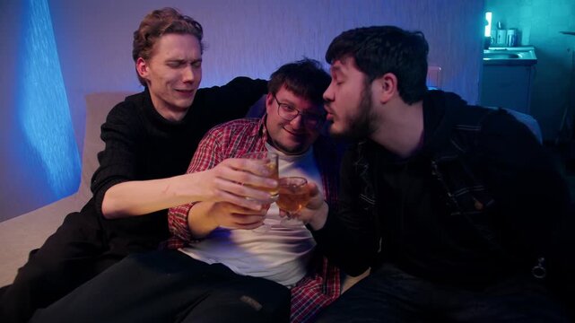Group of male friends having casual talk. Caucasian drunk men sit on couch, discuss and drink alcoholic beverages in glasses in cozy room. Alcohol addiction in the social circle of people.