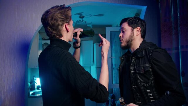 Playful hostile confrontation between two caucasian drunk men with bottles showing each other the finger. Nighttime kitchen standoff with attitude. Night scene of rivalry. Alcoholism and aggression