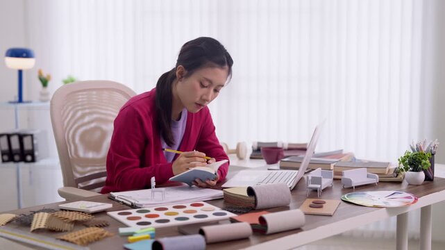 Asian furniture designer women planning interior design project writing notebook selecting material samples color palette workspace home office studio