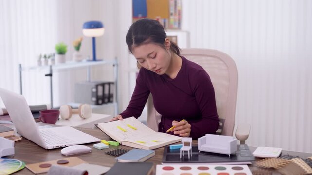 Asian woman furniture designer sketching product design blueprint working on creative project with color samples laptop home office studio workspace interior