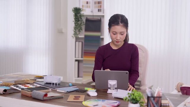 Asian furniture designer working on digital tablet designing products reviewing samples at home office desk creative professional planning interior decor