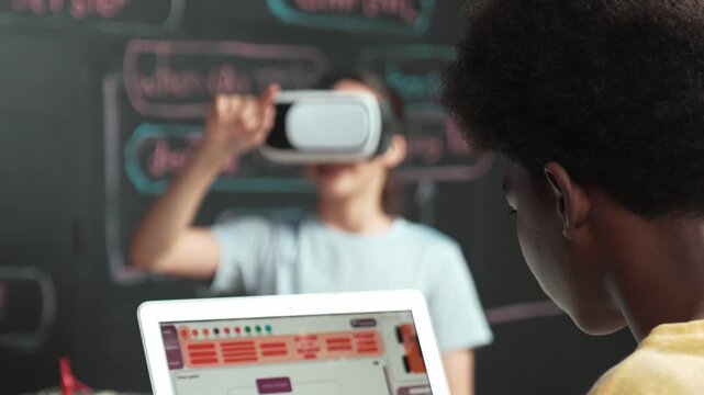 African boy programming system while caucasian girl enter metaverse while sitting at blackboard with engineering code written.high school girl wearing VR or headset in STEM technology. Edification