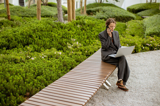 Man works on laptop in garden while talking on phone in urban setting