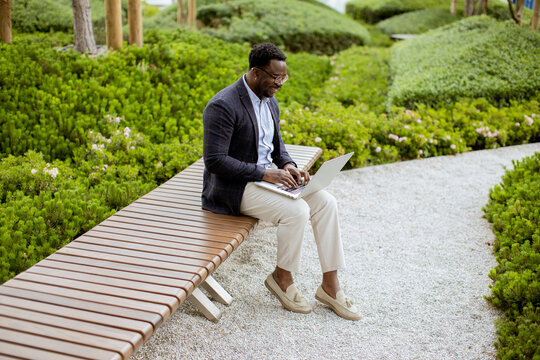 Man working on laptop in park with greenery during daytime hours in sunny weather