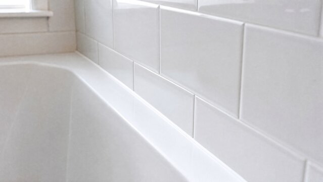 A clean white bathroom with a sealed bathtub and tile joint.