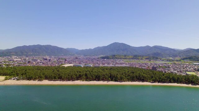 気比の松原（福井県敦賀市）の海と広大な松林、市街地と山並みのパノラマ、左へ横移動するドローン空撮 / Kehi no Matsubara in Tsuruga, Fukui: Panoramic drone aerial of sea, vast pine forest, city and mountains, tracking left