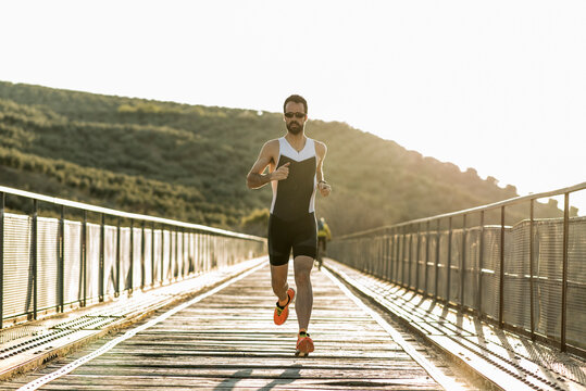 full length portrait of triathlon runner training at sunset on a bridge