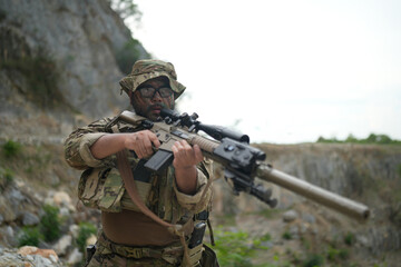 Fototapeta premium Soldier aiming a sniper rifle in a rocky, outdoor environment