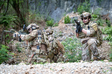Fototapeta premium Special forces soldiers in camouflage gear advance through a rocky, wooded terrain