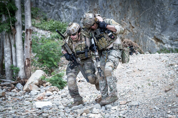 Fototapeta premium Soldiers assisting injured comrade during tactical training exercise in rocky terrain