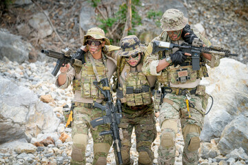 Fototapeta premium Special forces soldiers in camouflage gear assisting a wounded comrade in a rocky, outdoor environment