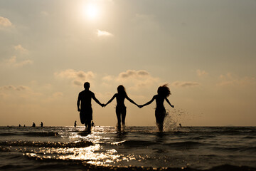 Fototapeta premium Silhouette, ocean and friends running at sunset for summer vacation, holiday and travel together outdoor. Beach, dusk and group of people at sea water for adventure, party and having fun in nature