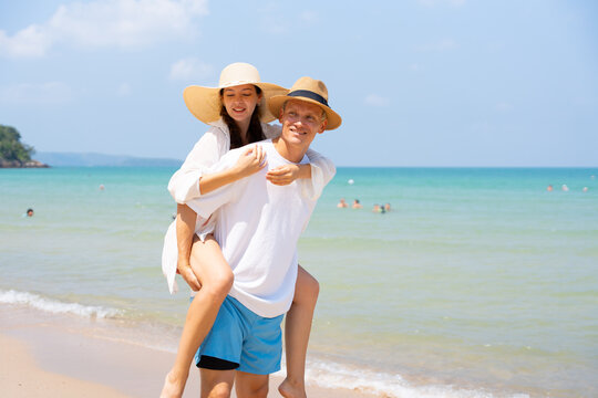 Romantic summer vacation concept. Happy young couple enjoying a piggyback ride by the tropical beach under clear blue sky, sharing love and carefree holiday moments. couple, beach, vacation, romance, 