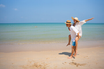 Fototapeta premium Romantic summer vacation concept. Happy young couple enjoying a piggyback ride by the tropical beach under clear blue sky, sharing love and carefree holiday moments. couple, beach, vacation, romance, 