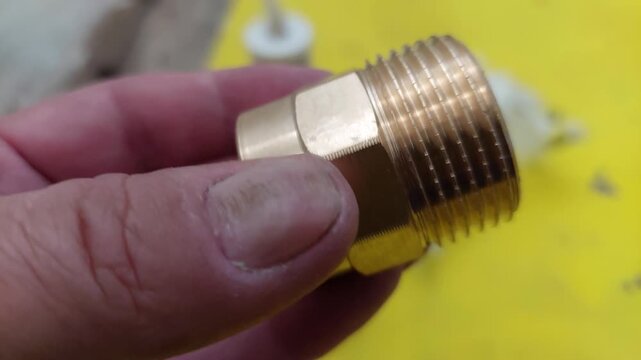 Plumber holding a new brass threaded nipple pipe fitting close up