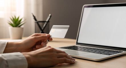 Fototapeta premium Hands holding a credit card near a laptop. Person making an online payment at a desk. E-commerce and digital banking concept
