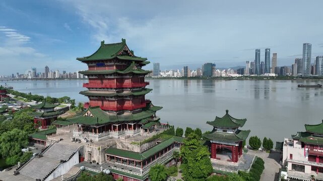 Aerial drone view Tengwang Pavilion, an ancient Chinese architectural masterpiece, stands prominently along the Gan River in Nanchang, China, with a modern city skyline and a blue sky in background