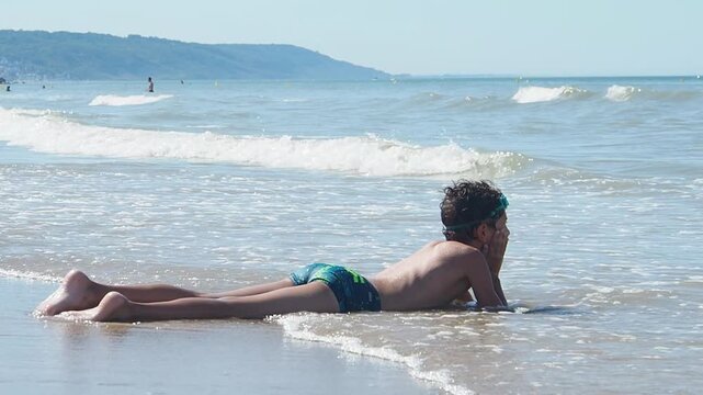 Child Relaxing in Shallow Sea Water as Waves Roll Ashore in Slow Motion