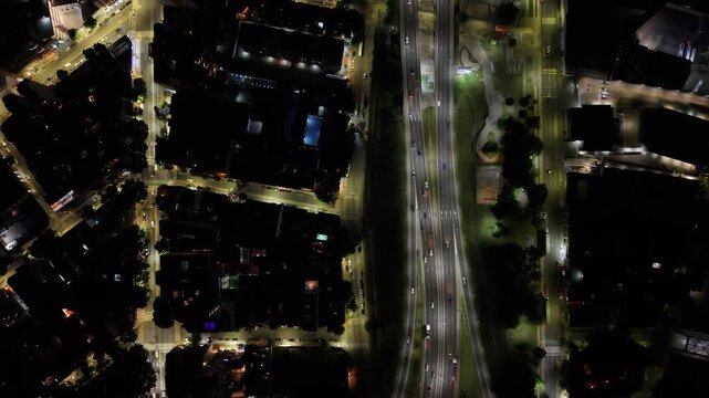 Vista cenital de una ciudad de noche descendiendo hasta un auto que dobla en una esquina, tr&aacute;fico urbano, calles iluminadas, dron