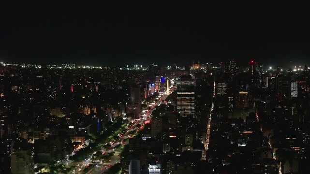 Vista a&eacute;rea nocturna con dron de la ciudad de Buenos Aires sobre la Avenida 9 de Julio y el Obelisco iluminado con tr&aacute;nsito urbano. Turismo, paisajes, porte&ntilde;o, ciudad magica.