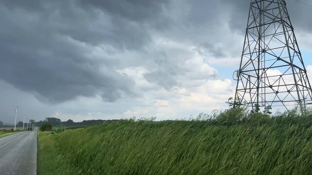 Storm clouds forming over a rural midwest road by a high voltage electrical tower in summer 