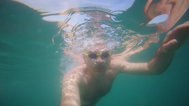 Dynamic underwater point of view footage of a swimmer moving through clear sea water
