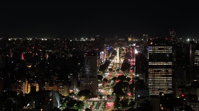 Vista a&eacute;rea nocturna con dron de la ciudad de Buenos Aires sobre la Avenida 9 de Julio y el Obelisco iluminado con tr&aacute;nsito urbano. Turismo, paisajes, porte&ntilde;o, ciudad magica.