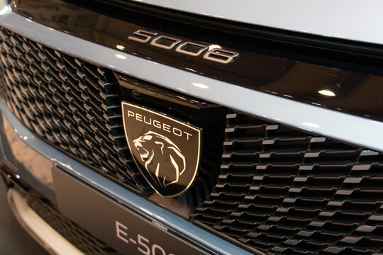 LISBON, PORTUGAL - MAY 16, 2026: Close-up angle view of the new lion shield emblem, textured matrix grille, and 5008 model badging on a grey Peugeot e-5008 electric SUV at the ECAR Show exhibition
