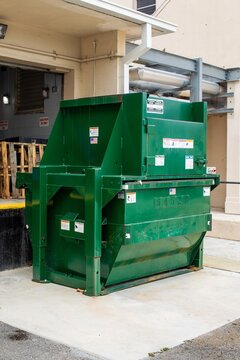 Small industrial green trash compactor in back of building