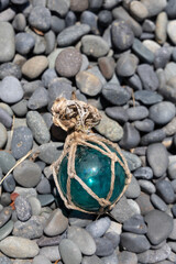 Vintage Japanese glass fishing floats and smooth gray pebbles piled together on a sandy beach by the ocean shore © Devka