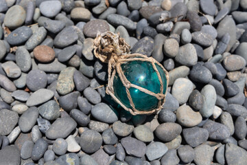 Vintage Japanese glass fishing floats and smooth gray pebbles piled together on a sandy beach by the ocean shore © Devka